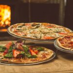 three specialty pizzas on a wooden table in front of a pizza oven | pizza West Roxbury