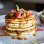 large stack of pancakes topped with fruit and syrup with butter on the side | breakfast West Roxbury